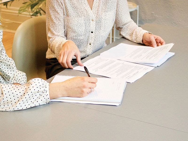 Two people sitting at a table with papers and pens.