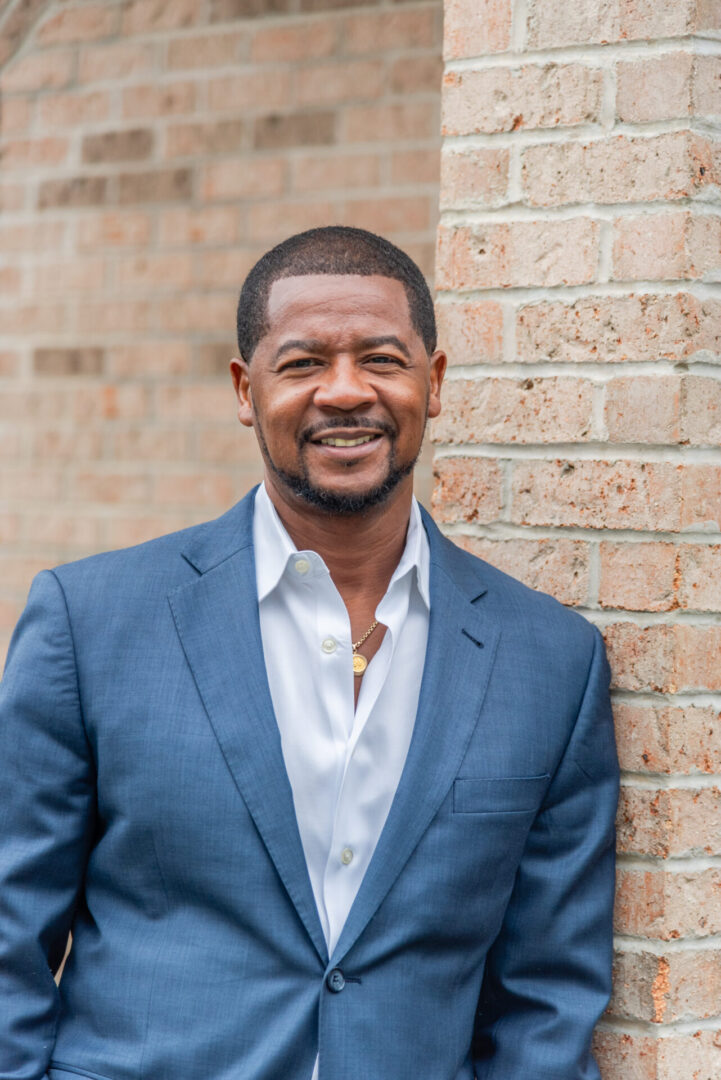 A man in a suit standing next to a brick wall.