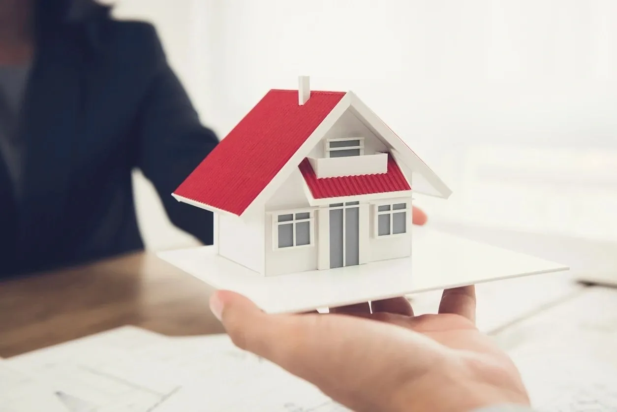 A person holding a paper house in their hand.