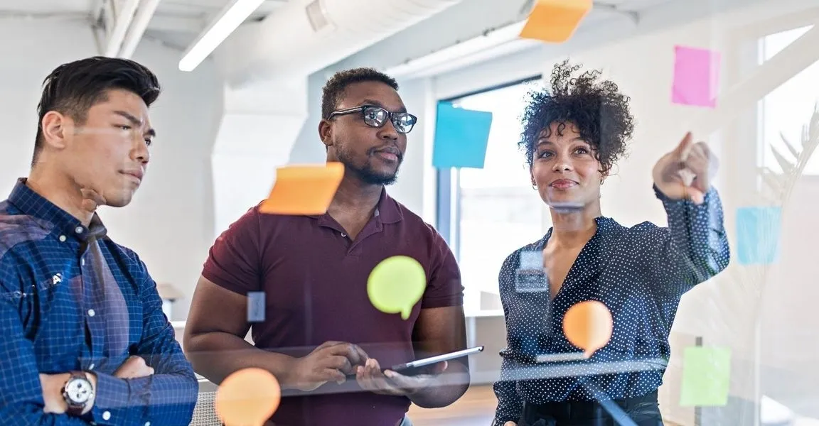 Two people are standing in a room with sticky notes on the wall.