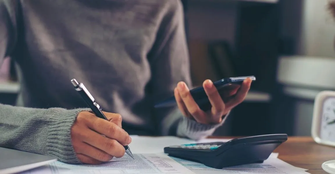 A person writing on paper with a pen and cell phone.