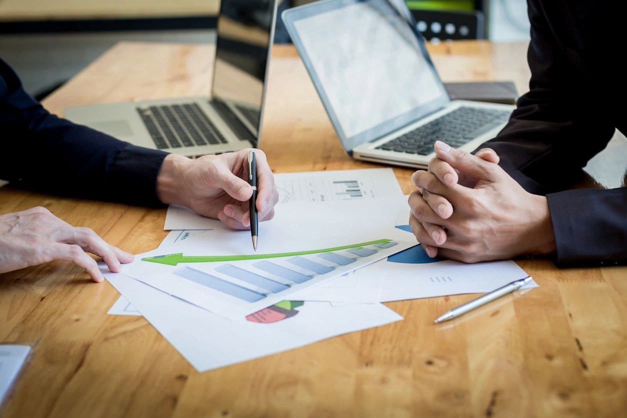 Two people are sitting at a table with papers and laptops.